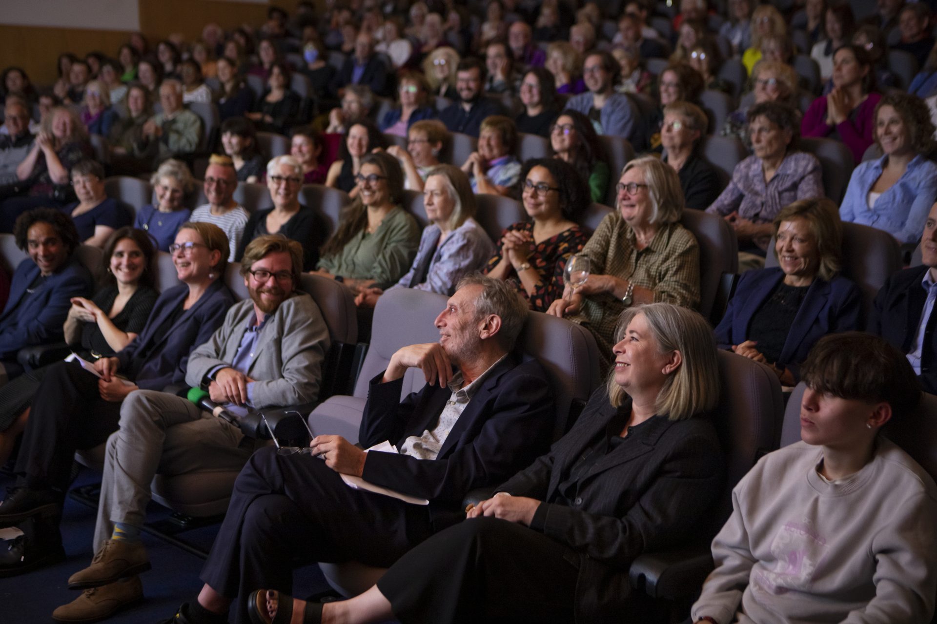 laughing audience members including Daniel Gorman and Michael Rosen seated at an event