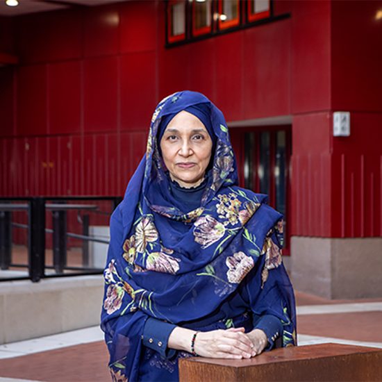 woman standing at a plinth wearing a blue floral head scarf