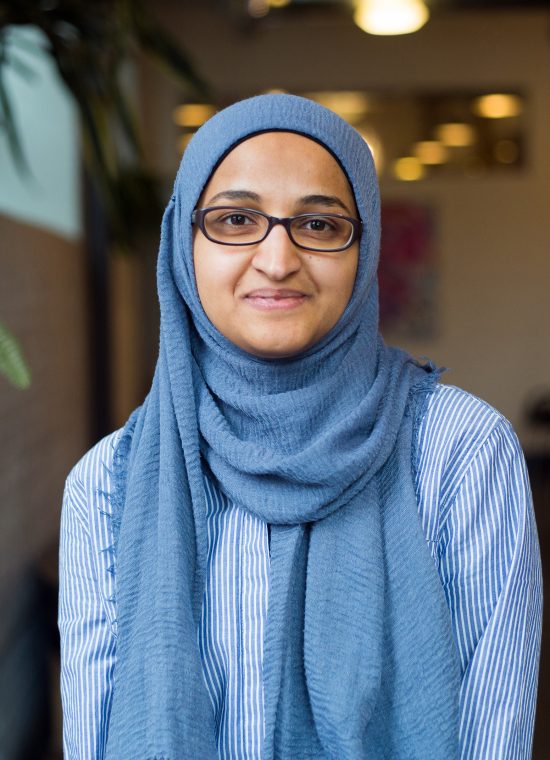 woman in glasses and a light blue head scarf standing in a softly lit space